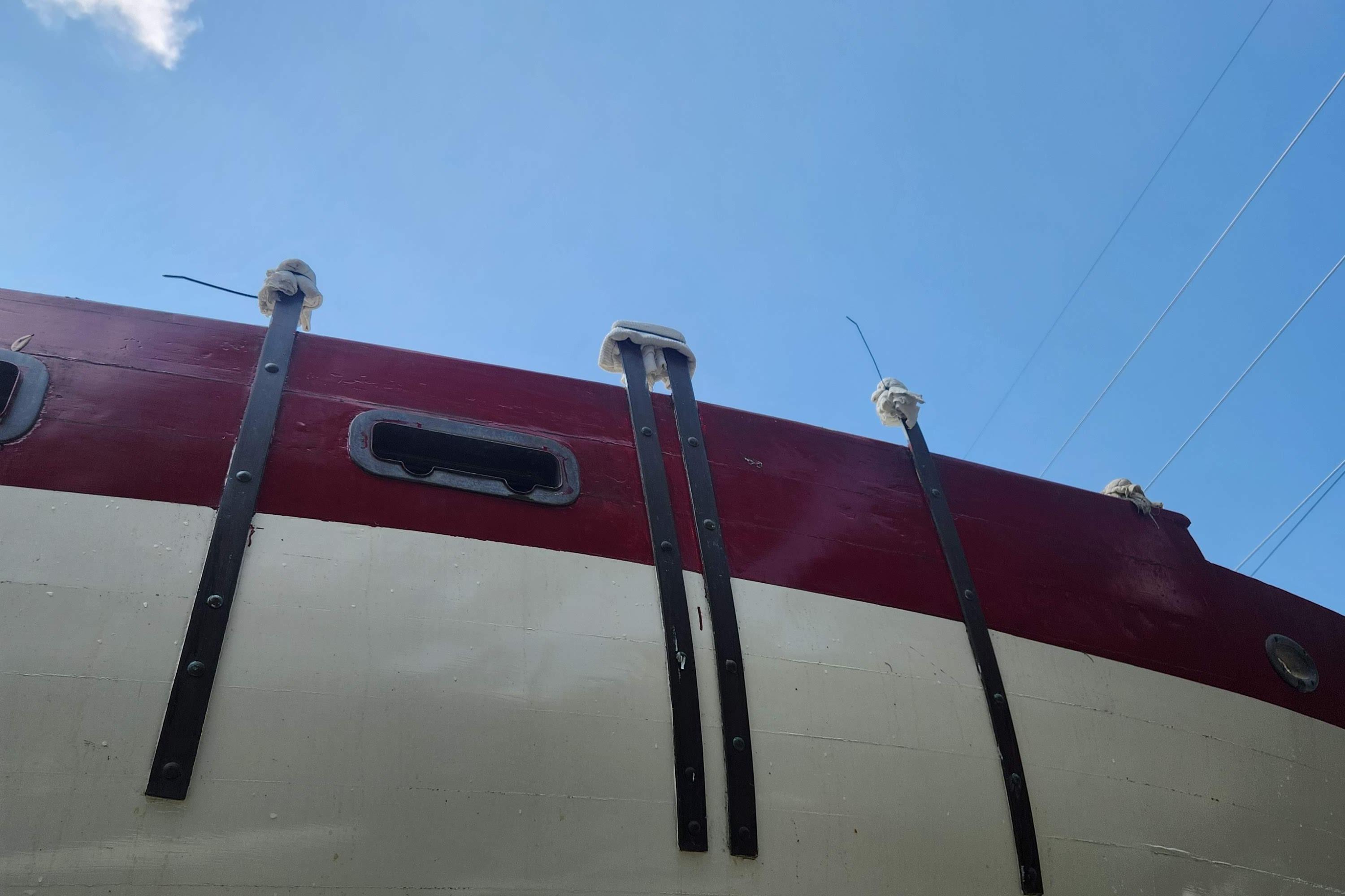 1959 Geerd Hendel Raised-Deck Cutter, red and white hull, viewed from below against blue sky.