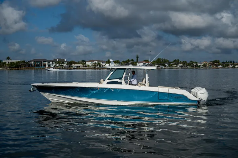  Yacht Photos Pics 2024 Boston Whaler 380 Outrage boat cruising on calm waters under cloudy skies.