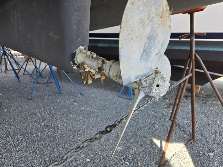 Surprise Yacht Photos Pics Propeller of a 2007 Beneteau 49 sailboat with marine growth, on a gravel surface.
