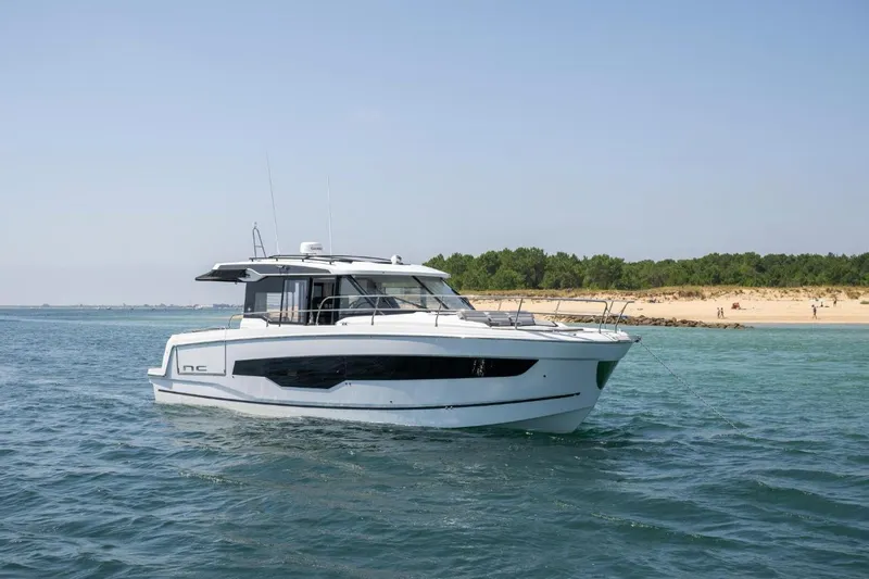  Yacht Photos Pics 2026 Jeanneau NC 1295 Weekender yacht on serene water near a sandy beach.