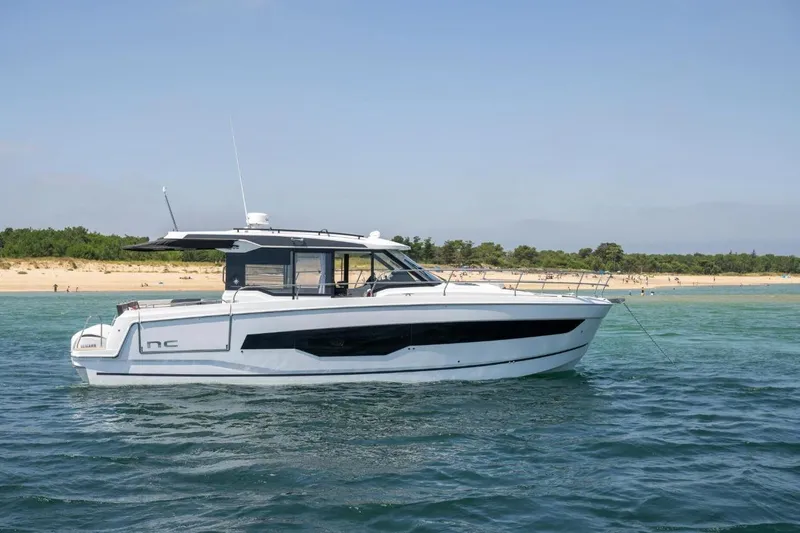  Yacht Photos Pics 2026 Jeanneau NC 1295 Weekender yacht cruising near a sandy beach.