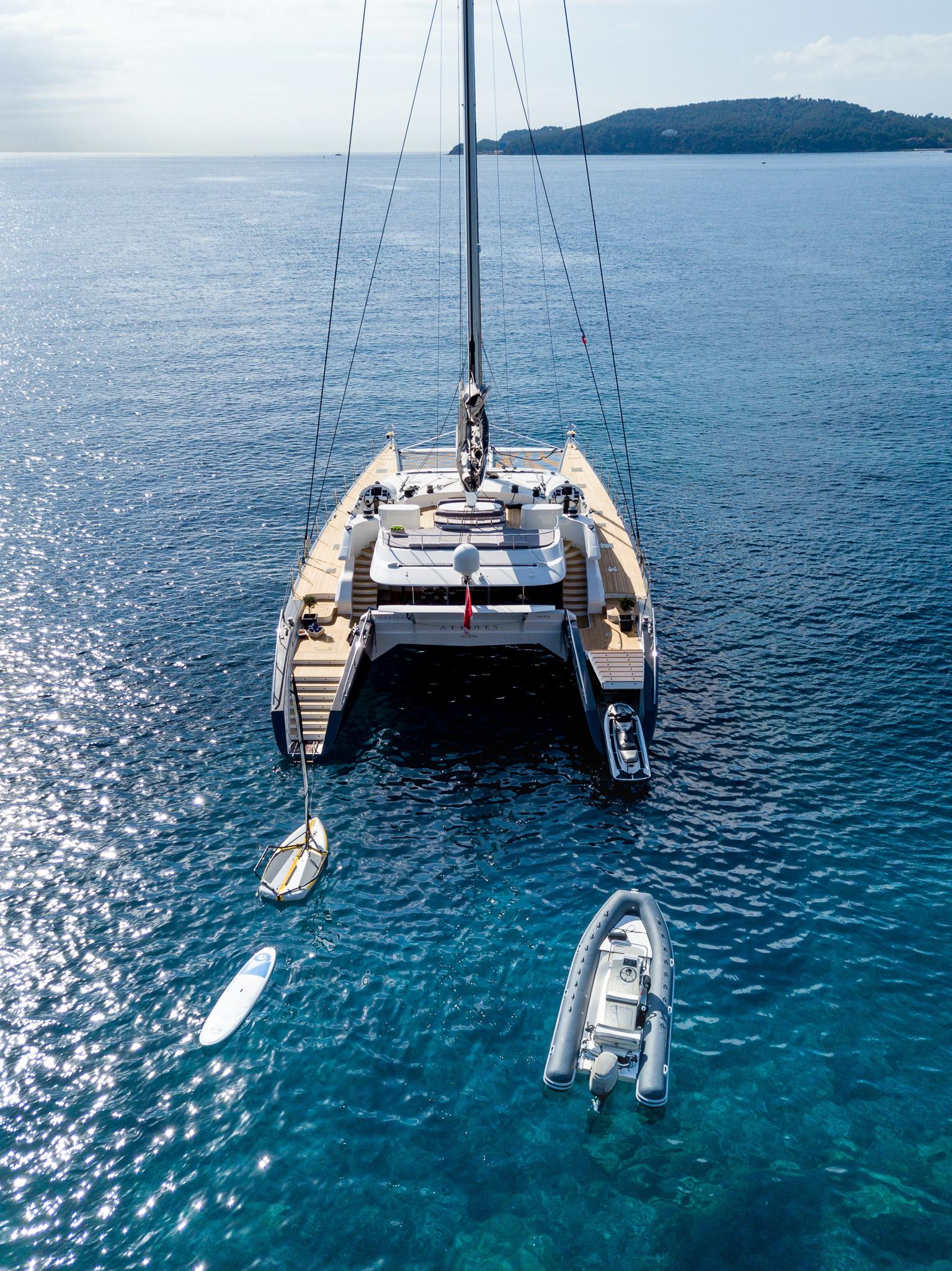 Luxury catamaran by Compositeworks (2006) with paddleboards and dinghy in serene ocean setting.