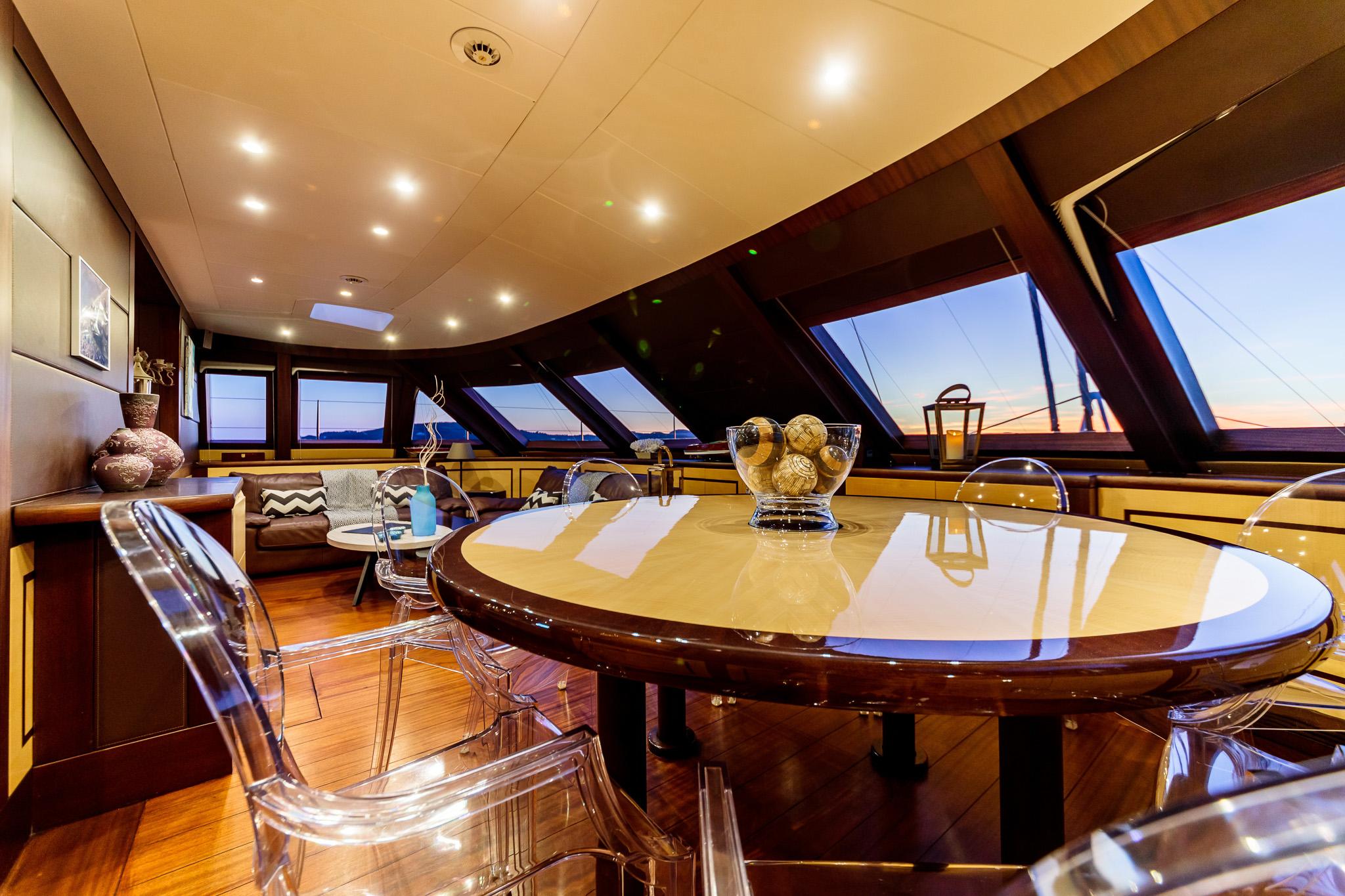 Luxurious yacht interior with elegant dining area, modern decor, and panoramic windows at sunset.