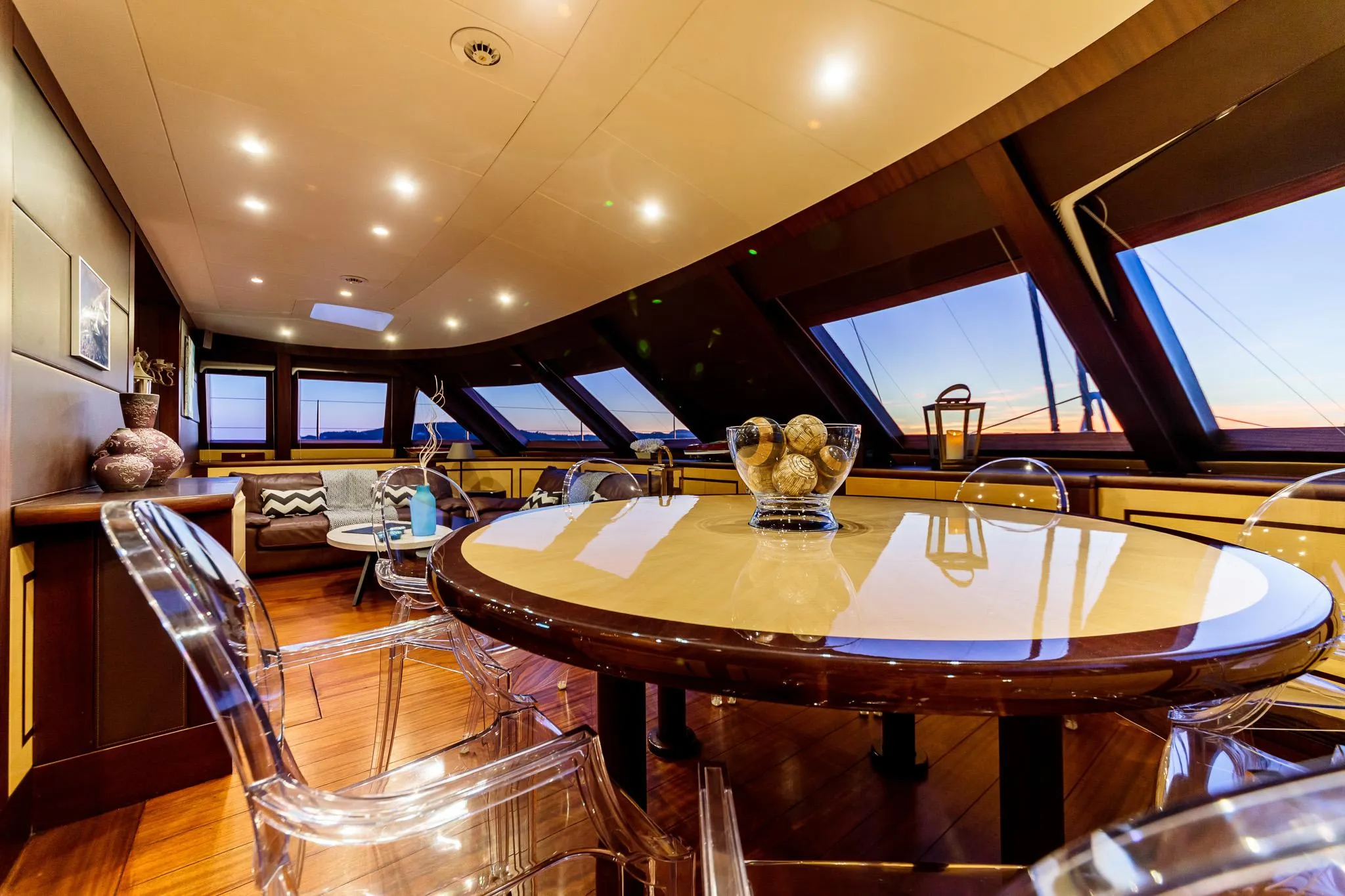Luxurious yacht interior with elegant dining area, modern decor, and panoramic windows at sunset.