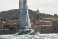 Sailing yacht by Compositeworks 2006 near coastal town with bell tower and hills.
