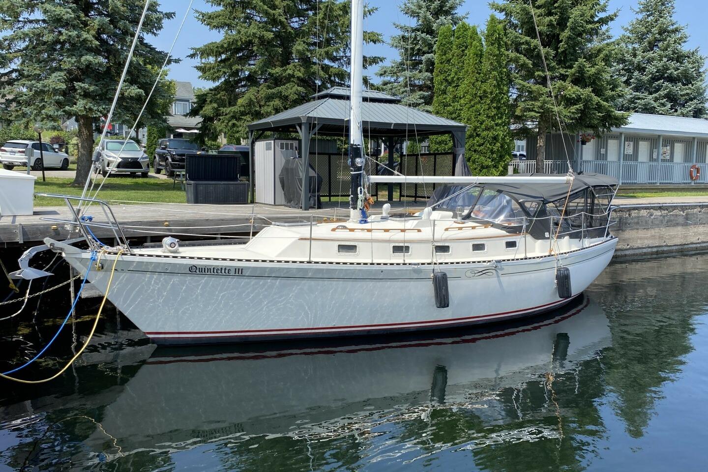 1984 Aloha 34 sailboat docked, surrounded by trees and parked cars.