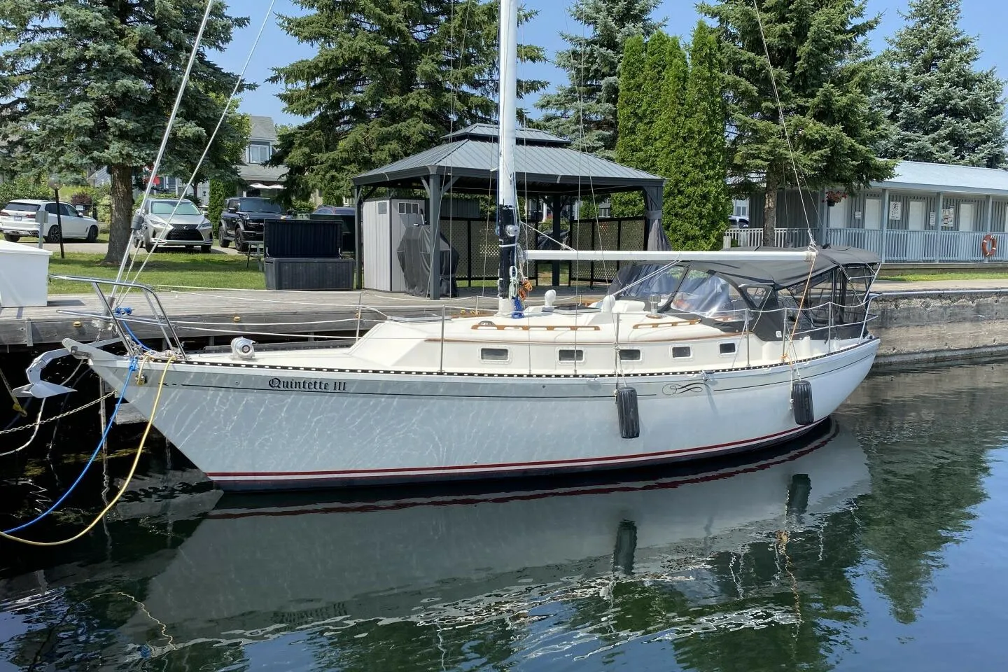 1984 Aloha 34 sailboat docked, surrounded by trees and parked cars.