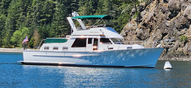 Westwind Yacht Photos Pics 2004 Westcoast 46 yacht on serene water, surrounded by lush forest and rocky cliffs.