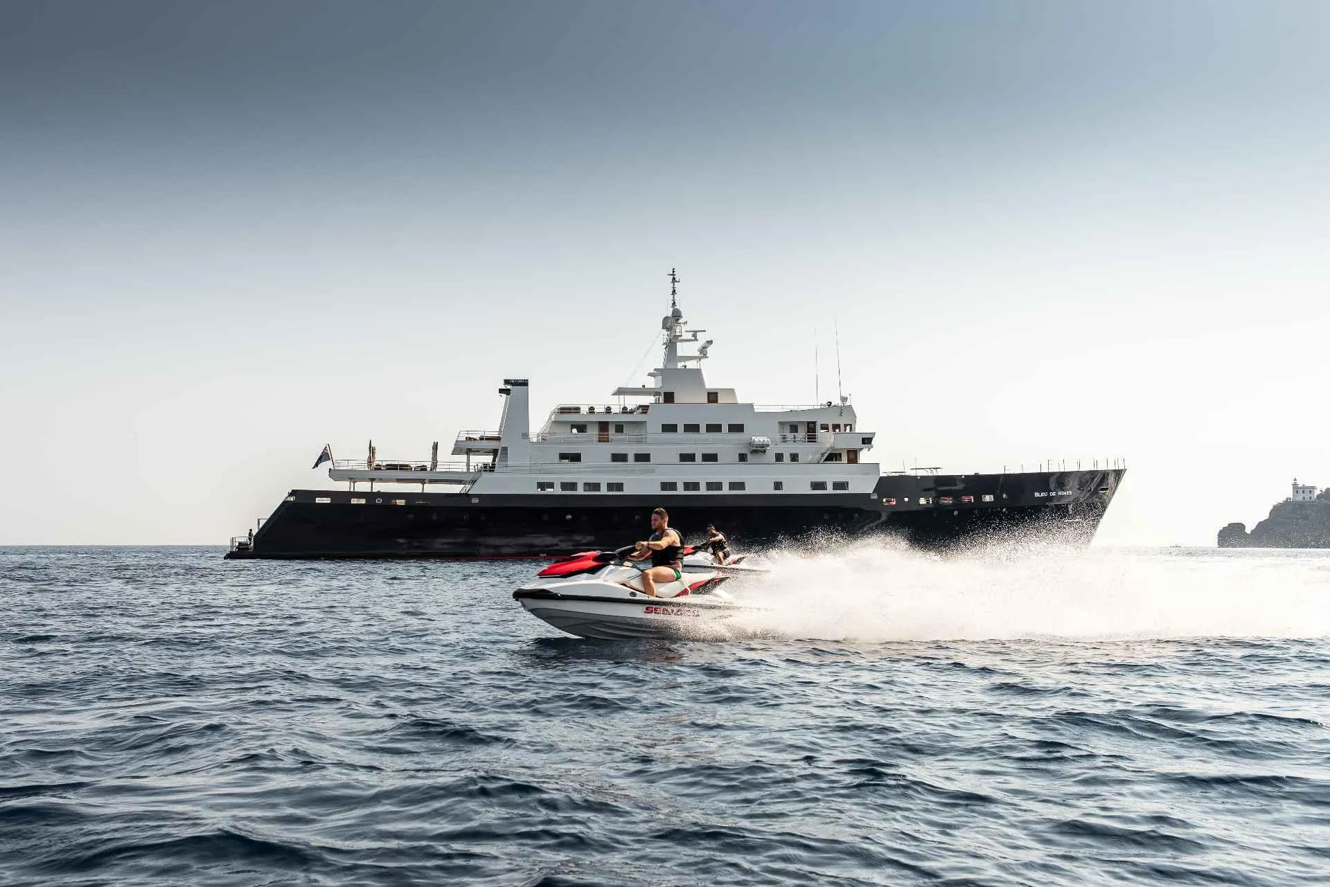 Jet ski speeding near a large custom conversion yacht, 1980 model, on open water.