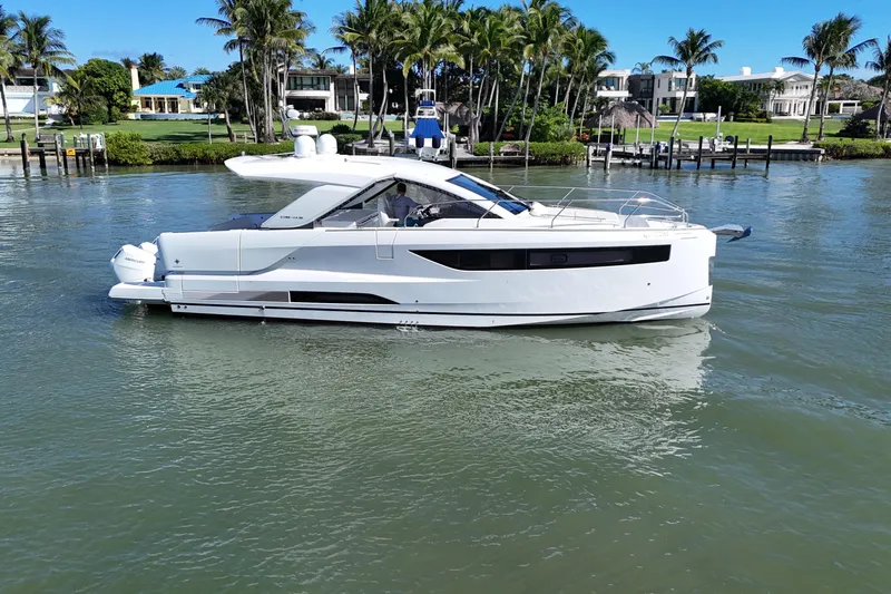  Yacht Photos Pics 2024 Jeanneau DB43 yacht cruising on a calm waterway with lush greenery in the background.
