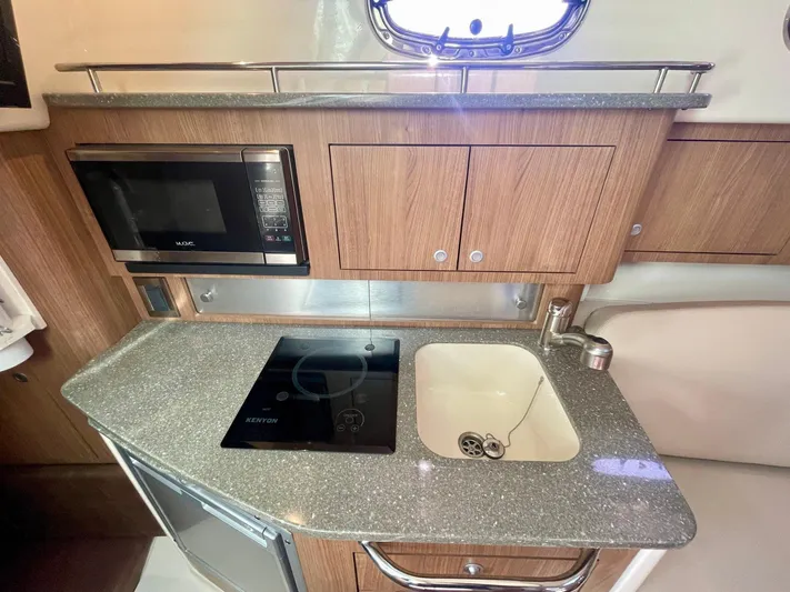 Strike Zone Yacht Photos Pics 2018 Boston Whaler 315 Conquest kitchen with microwave, stove, sink, and wooden cabinetry.