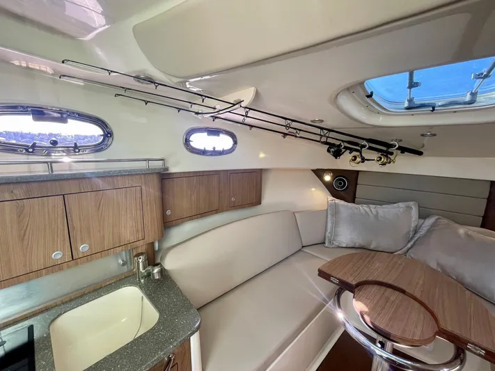 Strike Zone Yacht Photos Pics 2018 Boston Whaler 315 Conquest cabin interior with seating, table, and fishing rods.