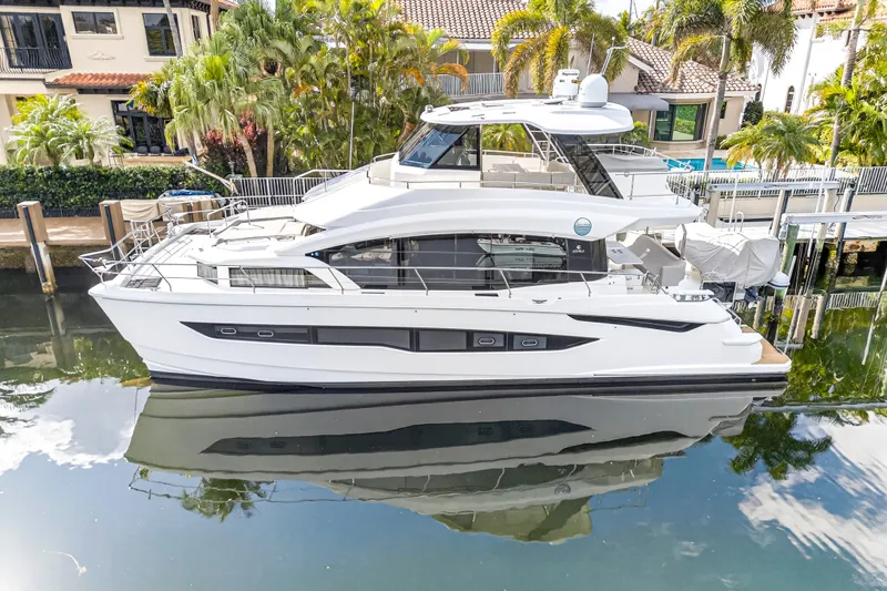  Yacht Photos Pics 2023 Aquila 54 Yacht docked, reflecting on calm water, surrounded by tropical greenery.