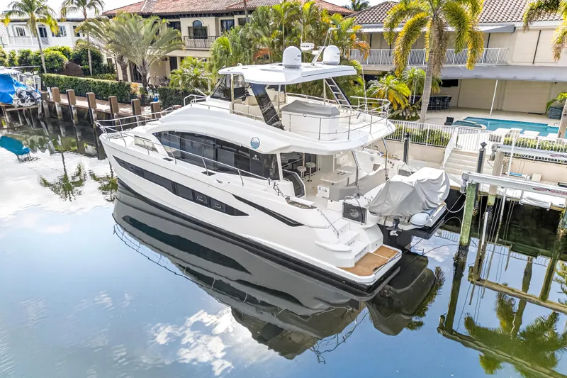  Yacht Photos Pics 2023 Aquila 54 Yacht docked in a serene waterfront setting with lush surroundings.