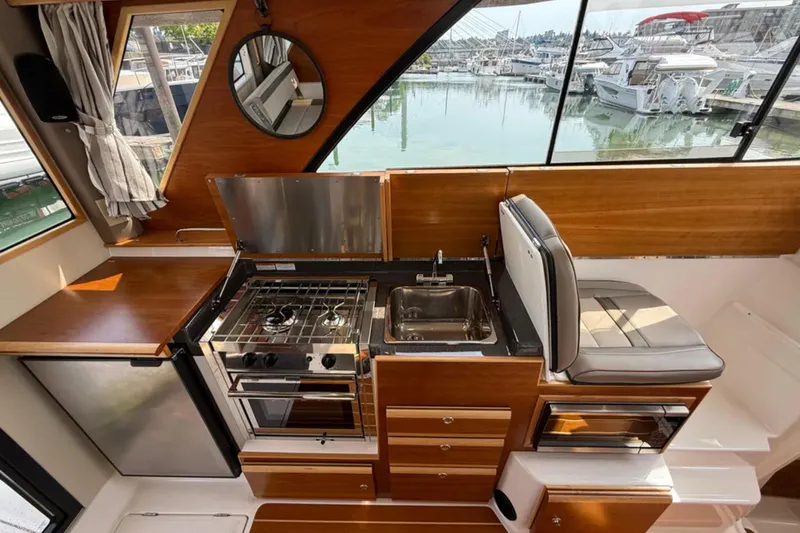  Yacht Photos Pics 2021 Cutwater C-32 Coupe interior with kitchen, stove, sink, and seating, overlooking marina.