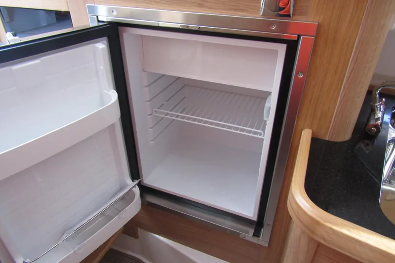  Yacht Photos Pics Open refrigerator inside 2025 Nimbus Commuter 11 boat, featuring wooden cabinetry and compact design.