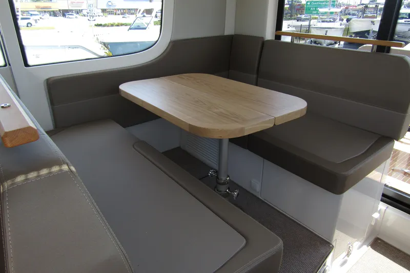  Yacht Photos Pics Interior seating area of 2025 Nimbus Commuter 11 with a wooden table and cushioned benches.