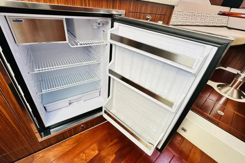  Yacht Photos Pics Open refrigerator inside 2022 Pursuit OS 355 Offshore boat, featuring wooden interior design.