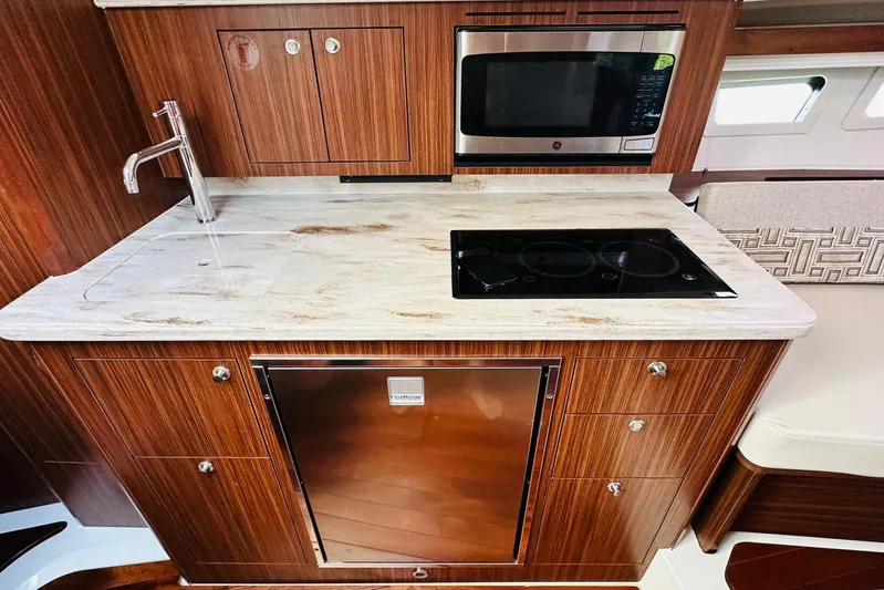  Yacht Photos Pics 2022 Pursuit OS 355 Offshore yacht kitchen with wood cabinetry, sink, microwave, and cooktop.
