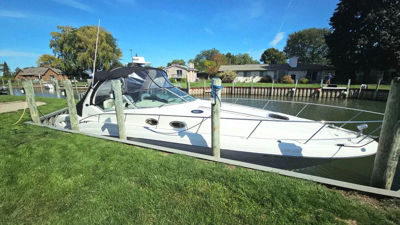  Yacht Photos Pics 2003 Sea Ray 340 Sundancer docked by a grassy shoreline under a clear blue sky.