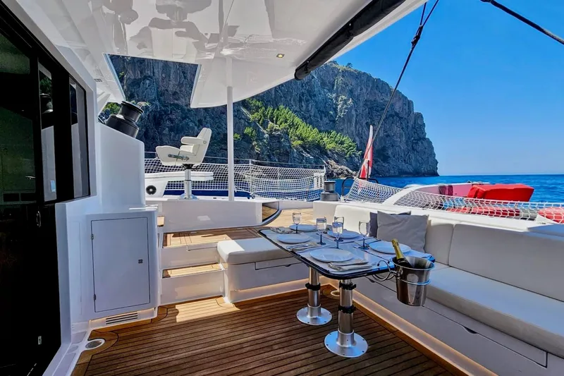  Yacht Photos Pics Luxurious 2016 HH66 catamaran deck with dining setup, ocean view, and rocky cliffs.