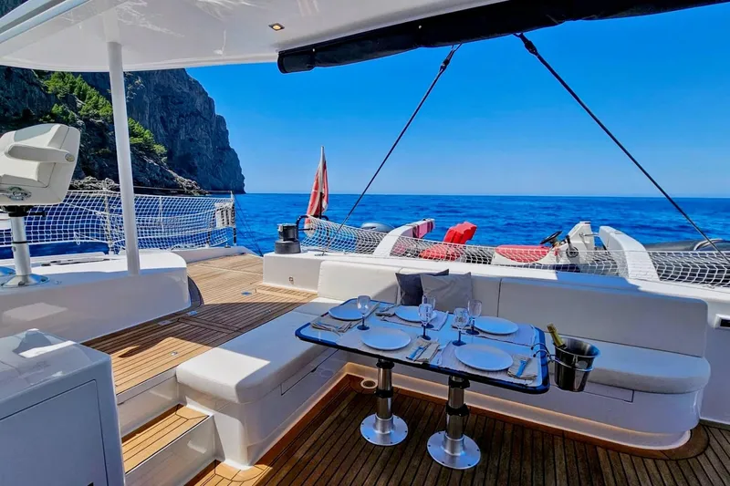  Yacht Photos Pics Luxurious 2016 HH Catamarans HH66 yacht deck with dining setup, ocean view, and coastal backdrop.