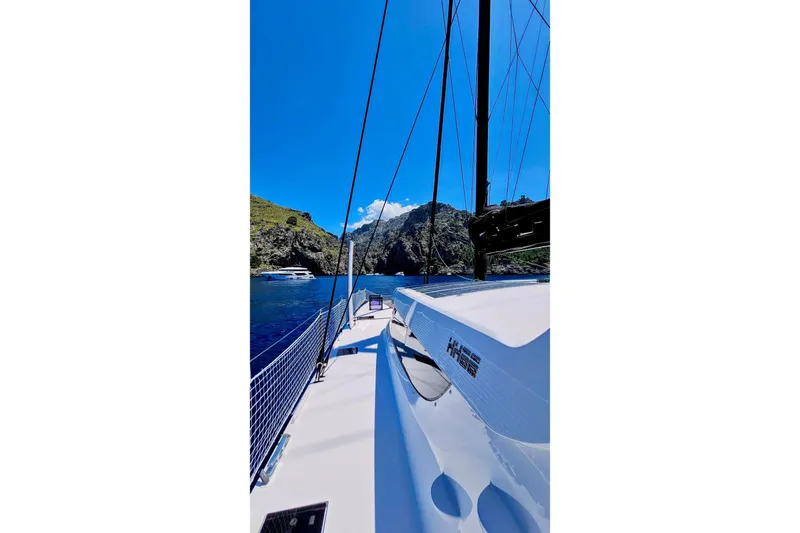  Yacht Photos Pics 2016 HH Catamarans HH66 sailing near rocky coastline under clear blue sky.