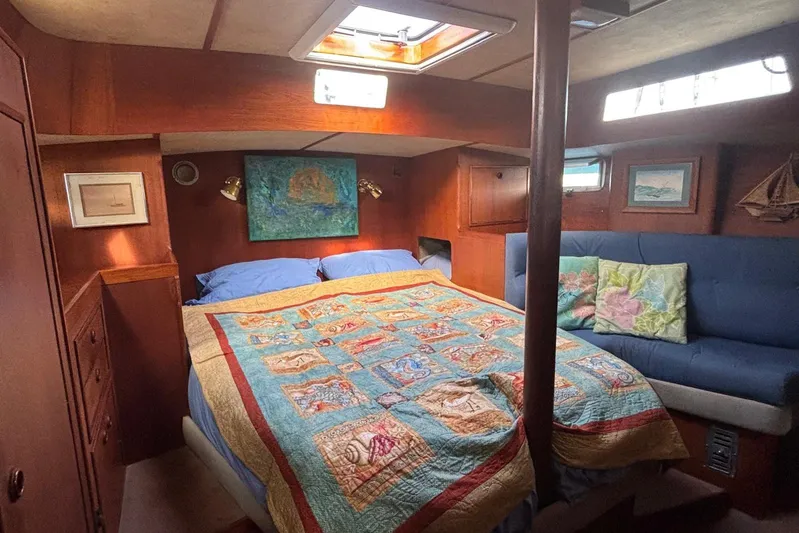 Prism Yacht Photos Pics Cozy cabin interior of 1984 Oyster 435 sailboat with colorful quilt and wooden furnishings.