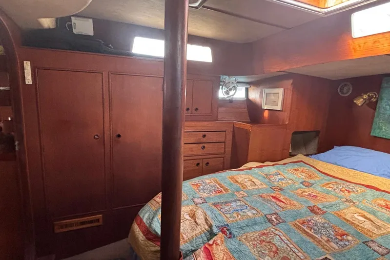 Prism Yacht Photos Pics Cozy cabin interior of 1984 Oyster 435 sailboat with colorful quilt and wooden furnishings.