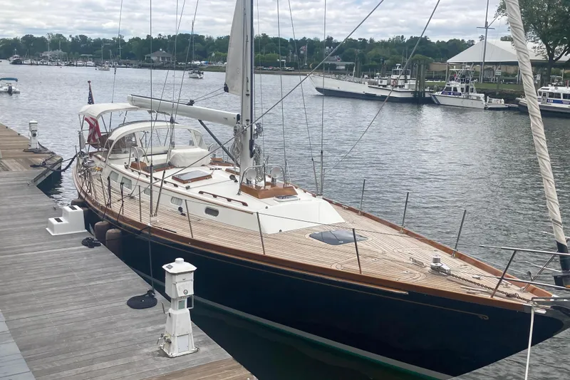 Symphony V Yacht Photos Pics Hinckley Sou'wester 52 sailboat docked, 1999 model, with wooden deck and white sails.