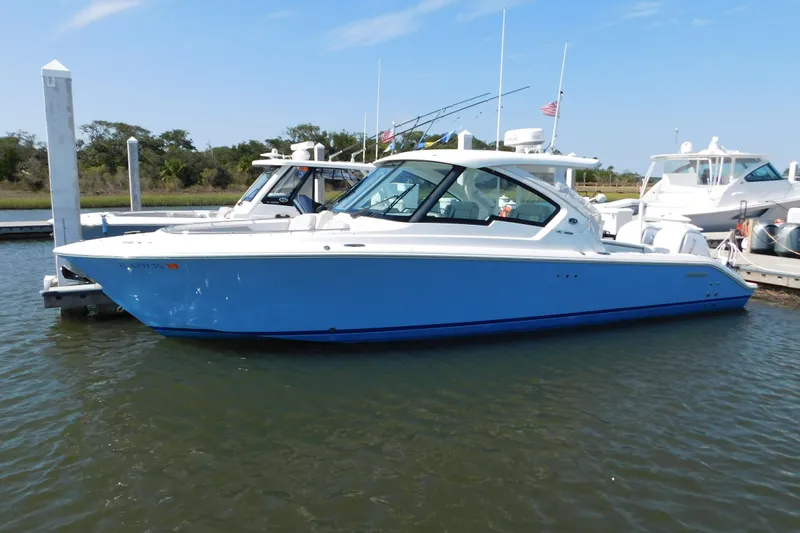  Yacht Photos Pics 2024 Pursuit DC 326 Dual Console boat docked in marina, blue hull, clear sky.