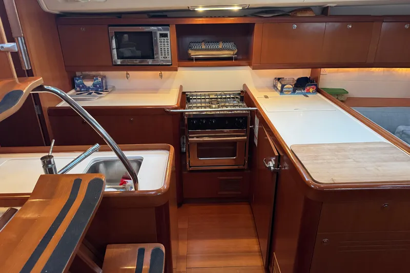 Lumiere Yacht Photos Pics 2007 Beneteau 49 yacht kitchen with wooden cabinetry, stove, microwave, and sink.