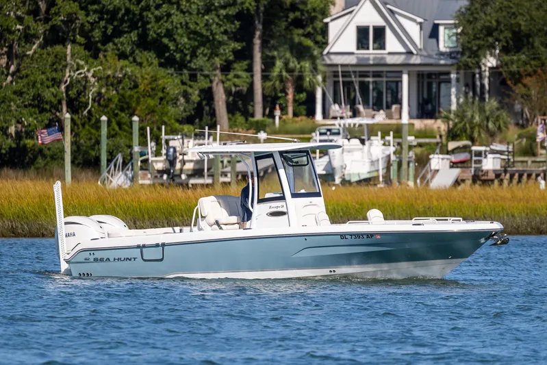  Yacht Photos Pics 2024 Sea Hunt Escape 28 boat cruising on a serene waterway near a coastal home.