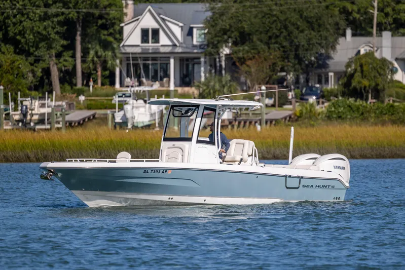  Yacht Photos Pics 2024 Sea Hunt Escape 28 boat cruising on a serene waterway near a coastal home.