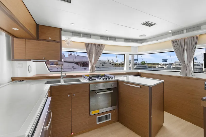 Happy Ours Yacht Photos Pics Modern kitchen interior of 2022 Lagoon 52 F yacht with wood cabinetry and large windows.