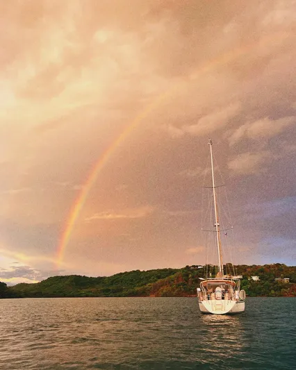 Via Yacht Photos Pics Sailboat Caliber 40 LRC SE 2004 under rainbow on serene water, lush green hills in background.