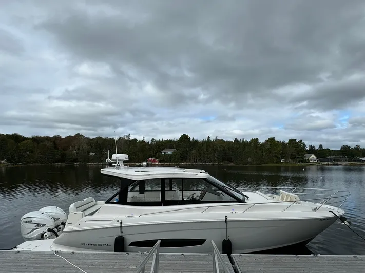 Harley Quinn Yacht Photos Pics 2023 Regal 36 XO boat docked on a serene lake under cloudy skies.