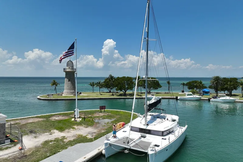 Rapscallion Yacht Photos Pics Lagoon 450 F catamaran docked near lighthouse, American flag waving, clear blue sky.