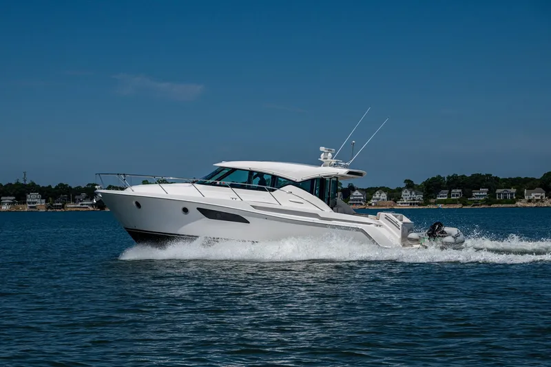  Yacht Photos Pics 2020 Tiara Yachts C44 Coupe cruising on a sunny day near coastal homes.