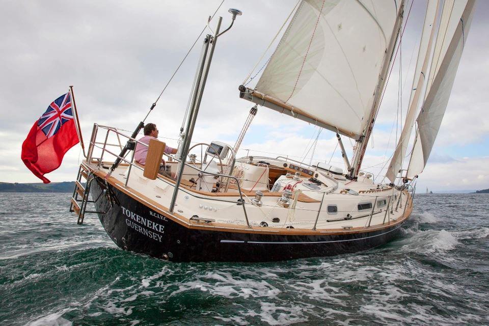 Sailing yacht Rustler 42, 2025 model, navigating ocean waters with a red ensign flag.