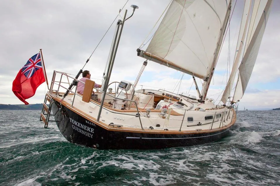 Sailing yacht Rustler 42, 2025 model, navigating ocean waters with a red ensign flag.