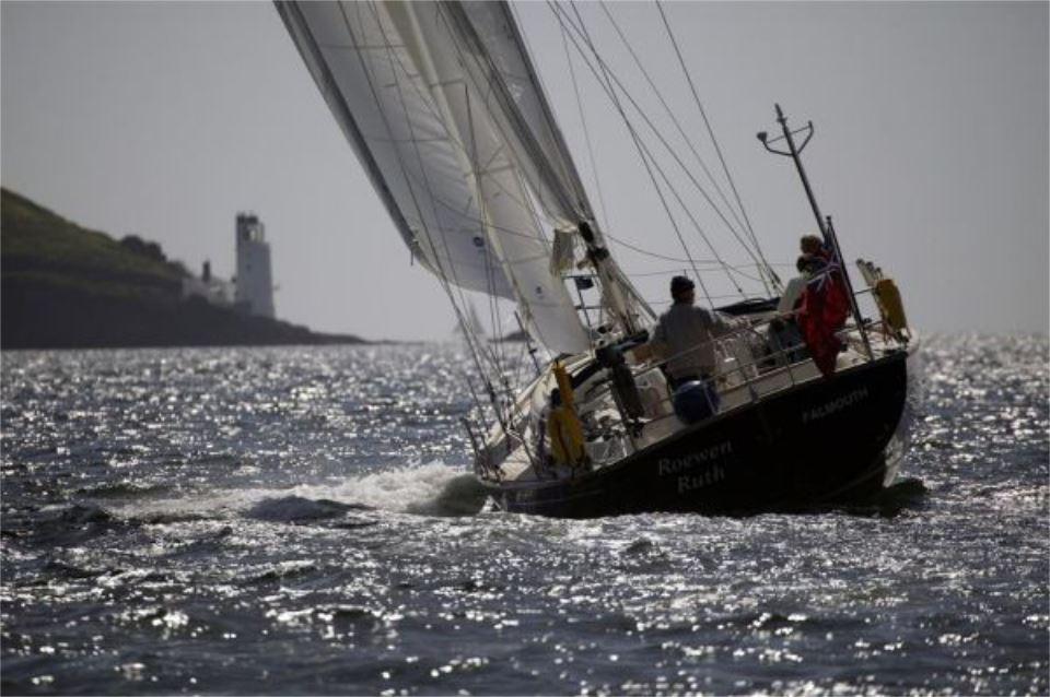 Sailing yacht Rustler 42, 2025 model, gliding on shimmering water near a lighthouse.