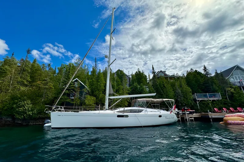 Porte Du Soleil Yacht Photos Pics 2015 Jeanneau Sun Odyssey 50 DS sailboat docked by lush green shoreline under a cloudy sky.
