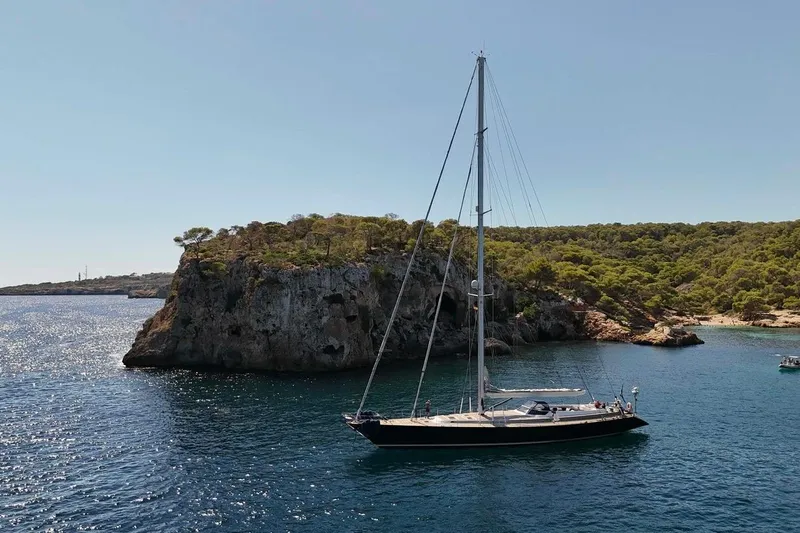 Persistence Yacht Photos Pics Sailboat "Sensation" from 1989 anchored near a rocky island with lush greenery.