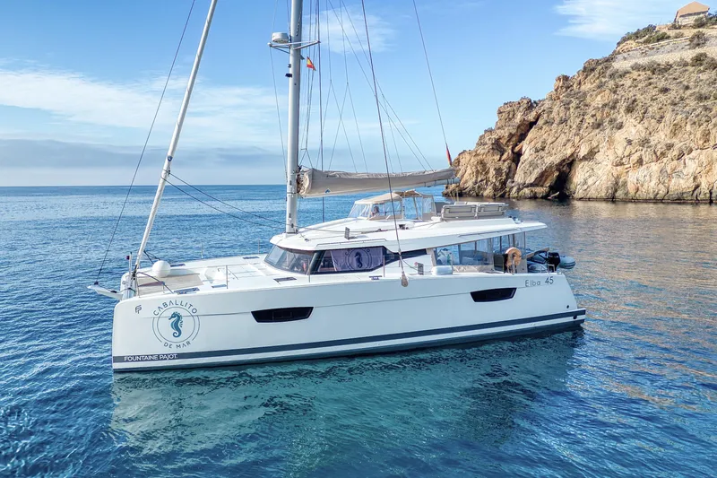 Cabalito De Mar Yacht Photos Pics 2024 Fountaine Pajot Catamaran Elba 45 sailing near rocky coastline.