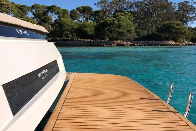  Yacht Photos Pics 2026 De Antonio Yachts D42 on serene turquoise waters near a lush shoreline.