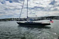Sailboat Rustler 33 (2017) on water, American flag, cloudy sky, marina background.