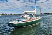 Sailboat Rustler 33, 2017 model, anchored in a scenic harbor under a partly cloudy sky.