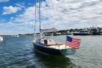 Sailboat Rustler 33 (2017) with American flag, docked in a scenic harbor under blue skies.