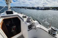 Sailboat Rustler 33 (2017) on water, with marina and cloudy sky in background.